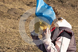 Little girl covered her face with Ukrainian blue-yellow flag, freedom concept