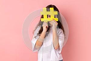 Little girl covering face with social media hashtag symbol, recommending to follow trendy content.