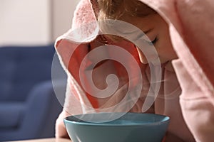 Little girl covering head with towel and inhaling steam indoors, closeup photo