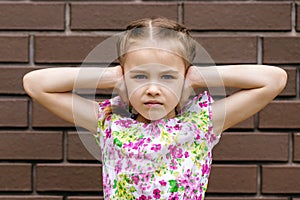 The little girl covers her ears with her hands and is unhappy with something