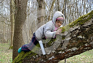 The little girl creeps on a trunk of a big tree in the spring wood