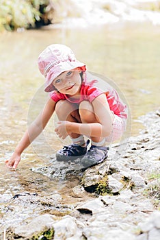 little girl crouches on the bank of the mountain stream