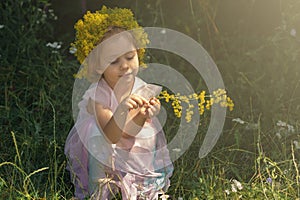 Little girl with crown of flowers playing in the forest. Summer time