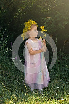 Little girl with crown of flowers playing in the forest. Summer time