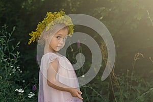 Little girl with crown of flowers playing in the forest. Summer time