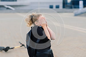 Little girl crying after she fell while riding her scooter at city street