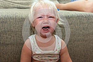 Little girl crying while sitting on the sofa in the room