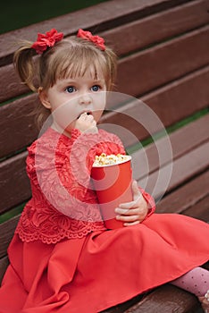 Little girl with cup of popcorn in park