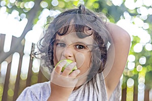 Little Girl with curly hair biting from an green apple