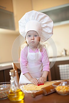 Little girl cuts dough for cookies on kitchen