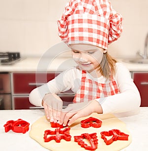 Little girl cuts dough with form for cookies