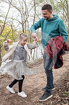 Little girl dances, holding dad`s hand on a walk in the woods