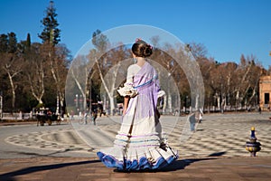 a little girl dancing flamenco dressed in a beige dress with ruffles and purple fringes in a famous square in seville, spain. The photo