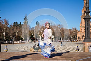 a little girl dancing flamenco dressed in a beige dress with ruffles and purple fringes in a famous square in seville, spain. The photo