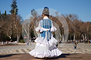 a little girl dancing flamenco dressed in a white dress with ruffles and blue fringes in a famous square in seville, spain. The