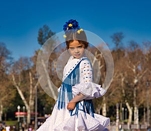 a little girl dancing flamenco dressed in a white dress with ruffles and blue fringes in a famous square in seville, spain. The photo