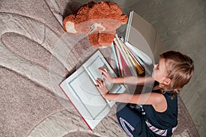 little girl in dark blue dress reading book sitting on the floor near teddy bear. Child reads story for toy.