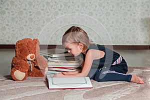 Little girl in dark blue dress reading book sitting on the floor near teddy bear. Child reads story for toy.