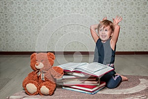 little girl in dark blue dress reading book sitting on the floor near teddy bear. Child reads story for toy. Showing bunny ears.