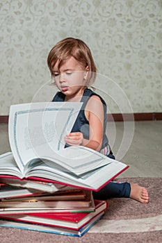 little girl in dark blue dress reading book sitting on the floor near teddy bear. Child reads story for toy. Turns the page.