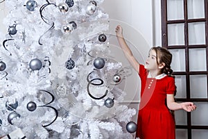 Little girl decorates the Christmas tree in red dress