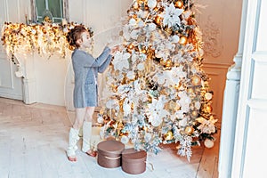 Little girl decorating Christmas tree on Christmas eve at home. Young kid in light bedroom with winter decoration. Happy family at