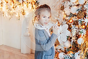 Little girl decorating Christmas tree on Christmas eve at home. Young kid in light bedroom with winter decoration. Happy family at