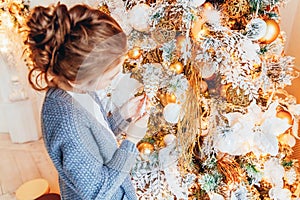 Little girl decorating Christmas tree on Christmas eve at home. Young kid in light bedroom with winter decoration. Happy family at