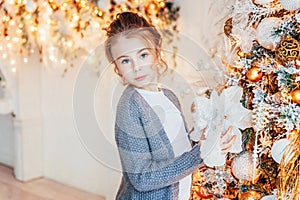 Little girl decorating Christmas tree on Christmas eve at home. Young kid in light bedroom with winter decoration. Happy family at