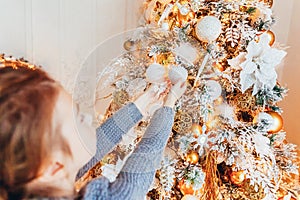 Little girl decorating Christmas tree on Christmas eve at home. Young kid in light bedroom with winter decoration. Happy family at