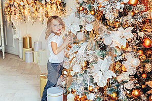 Little girl decorating Christmas tree on Christmas eve at home. Young kid in light room with winter decoration. Happy family at