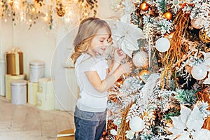 Little girl decorating Christmas tree on Christmas eve at home. Young kid in light room with winter decoration. Happy family at