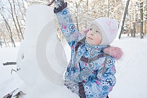 Little girl decorating winter snowman