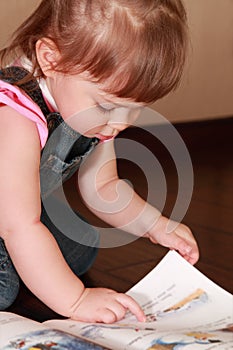 Little girl in denim jumpsuit reads book