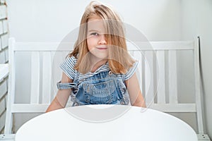 Little girl in denim sits on white bench at table. bright workplace for child