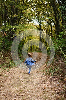 A little girl in a denim suit runs along a forest path.