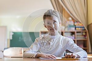 little girl at the desk is writing. education and school concept - little student girl writing in notebook at school