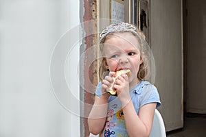Little girl in diadem hungrily bites sandwich photo