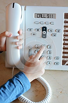 Little girl dialing 911 number on white landline phone