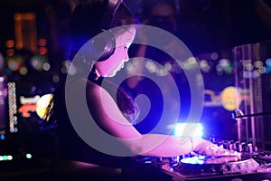 Little girl DJ playing live set and mixing music on controller turntable console mixing desk at stage in the night club, music
