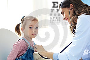 Little girl at the doctor for a checkup. Doctor woman auscultate the heartbeat of the child photo