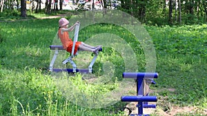 Little girl does exercises on outdoor exerciser in green park