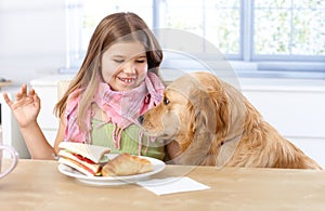 Little girl and dog at table having lunch smiling