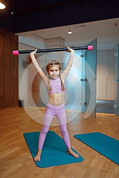 Little girl doing exercise with bar on mat in gym