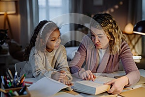 Little girl doing homework with her mother in evening at home.