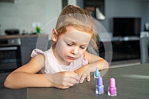 Little girl doing manicure and painting nails with colorful pink, blue and purple nail polish at home.