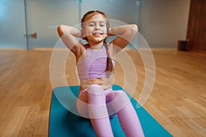 Little girl doing press exercise on mat in gym