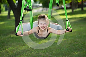 Little girl doing yoga exercises with a hammock in the park.