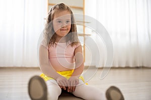 Little girl with down syndrome at ballet class in dance studio,sitting and resting. Concept of integration and education