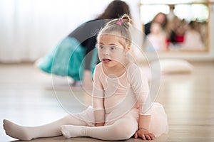 Little girl with down syndrome at ballet class in dance studio,sitting and resting. Concept of integration and education